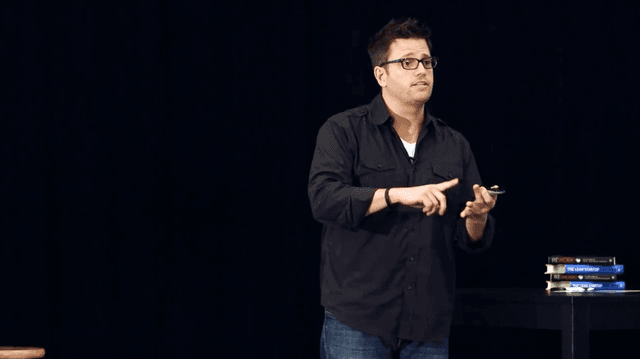 Rob Scott speaking on stage, confident and at ease, with books visible nearby
